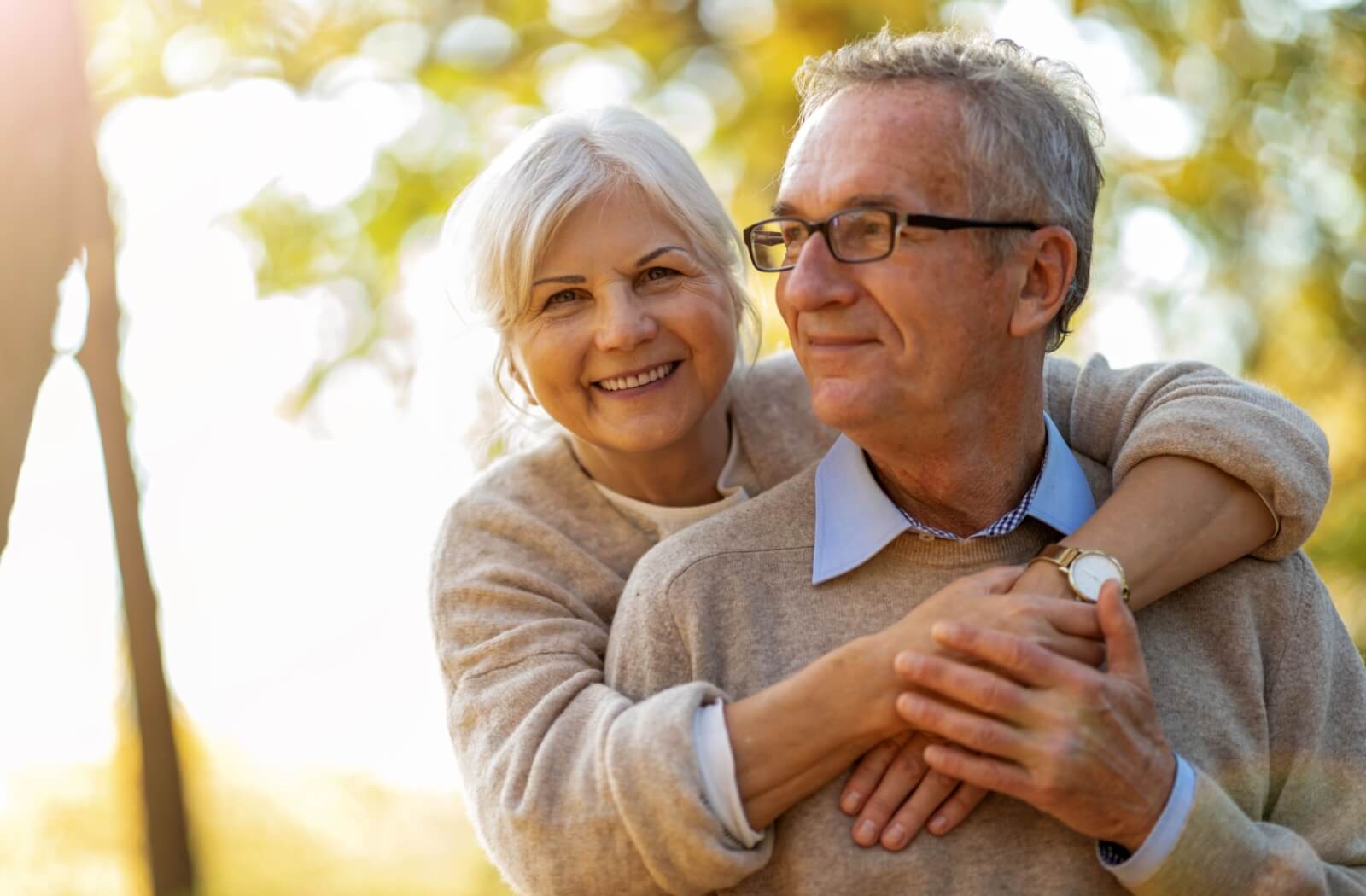 An older adult hugging their spouse from behind while the sun shines in senior living.