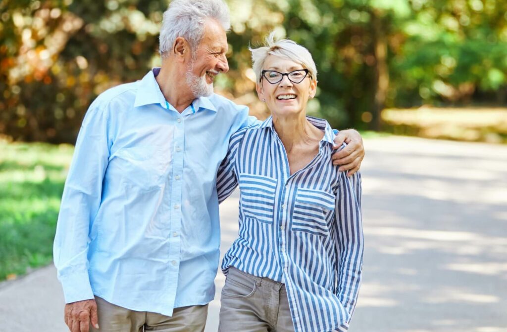 An older couple walking down the path in senior living with arms around one another while they smile.