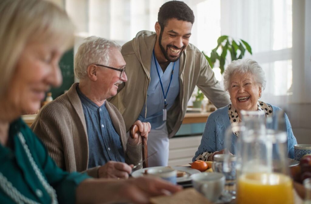 A caregiver in senior living checking in on a group of happy residents during a community meal.