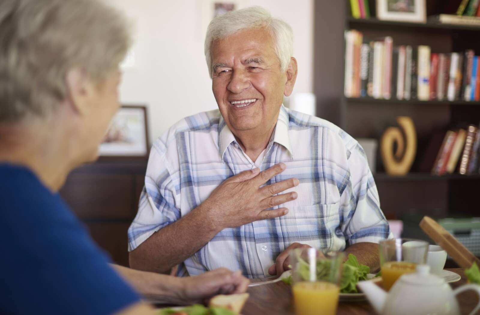 n older adult smiles while enjoying a meal with another resident in their senior living community.