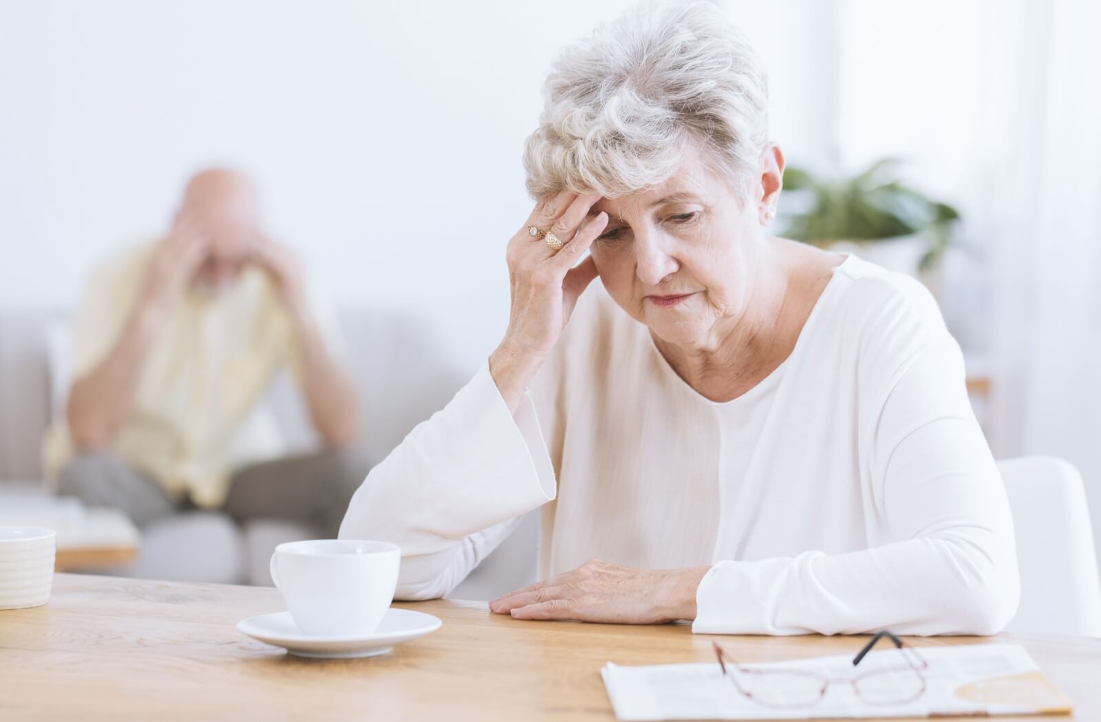 An older adult rubbing their forehead and trying to remember something at their table in personal care.