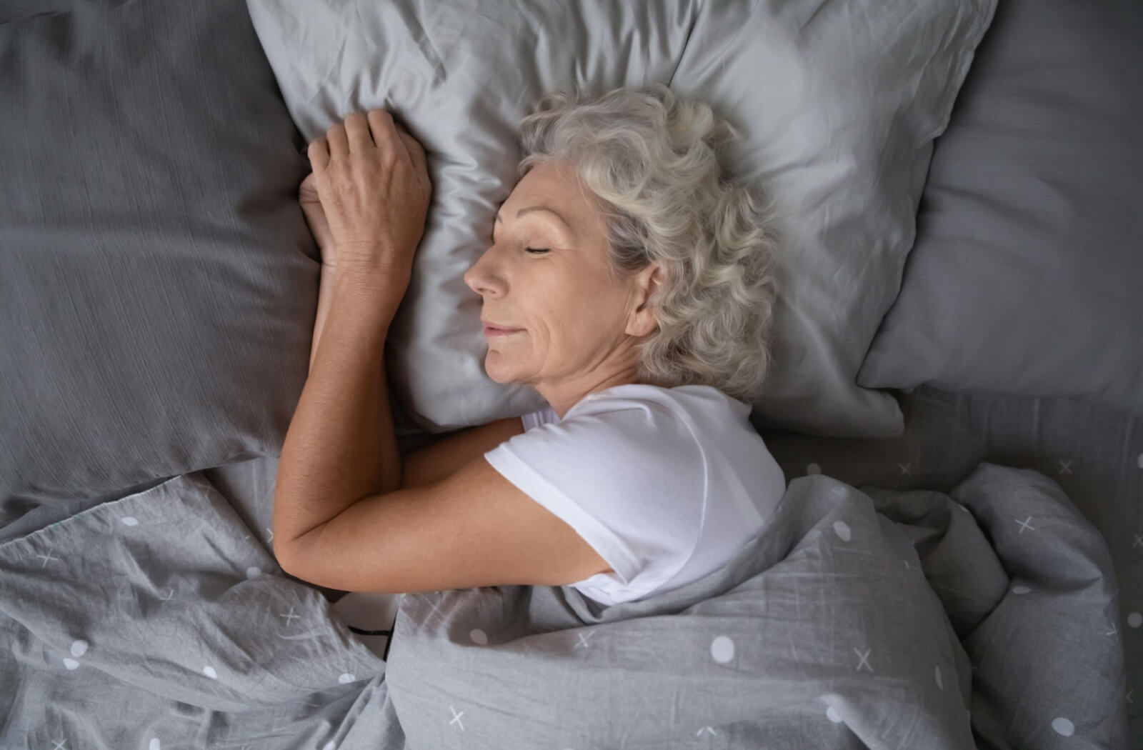 An overhead shot of an older adult lying in bed and sleeping.