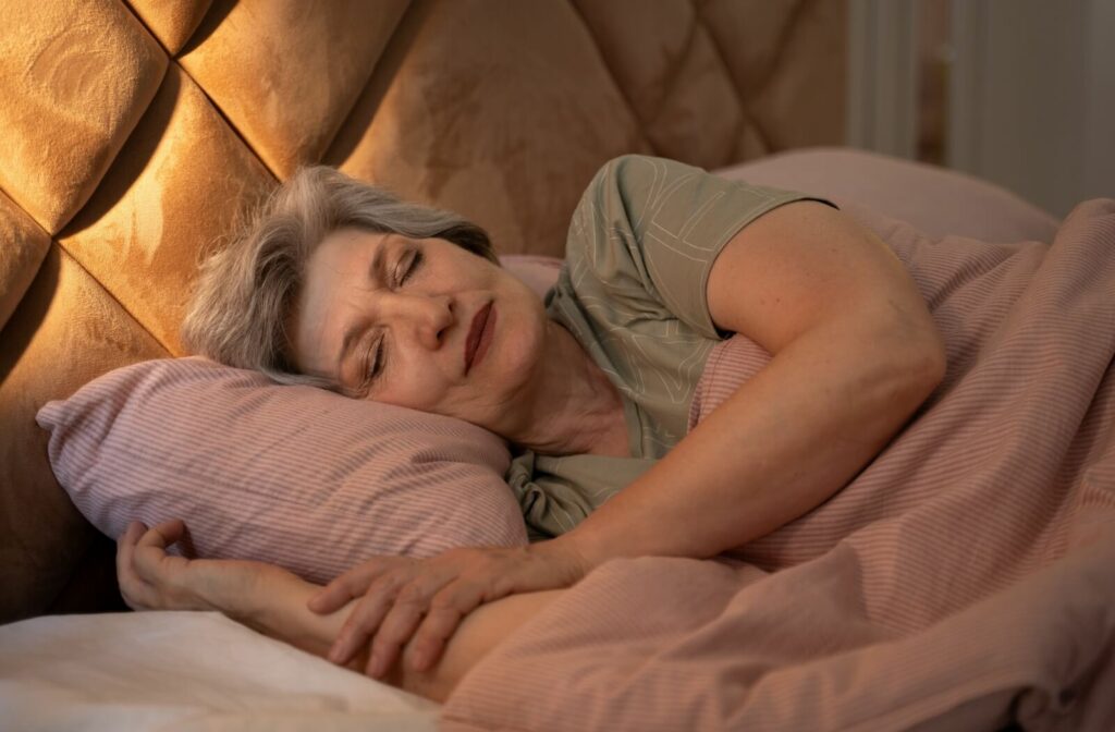 An older adult smiles as they sleep in a dim bedroom.