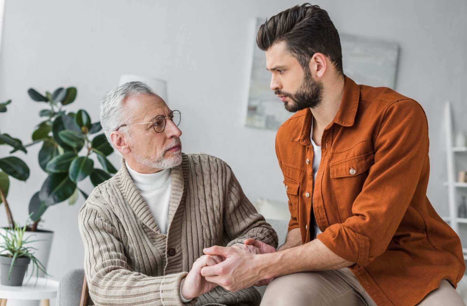 An adult child holding their aging parent's hands to support them during a stressful episode.