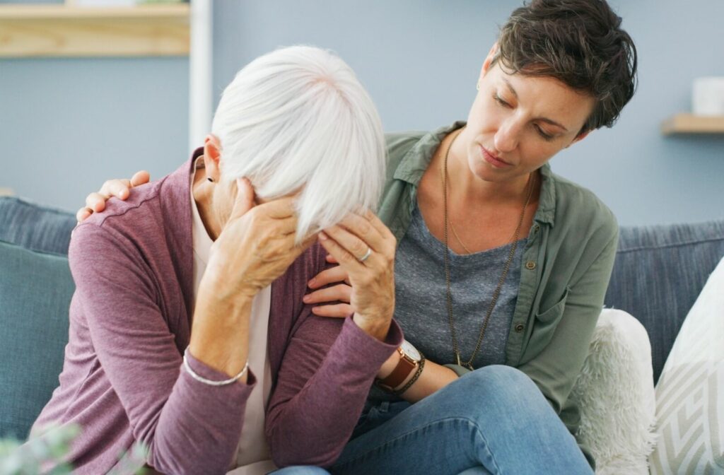 An adult child supporting their stressed older parent on the couch.