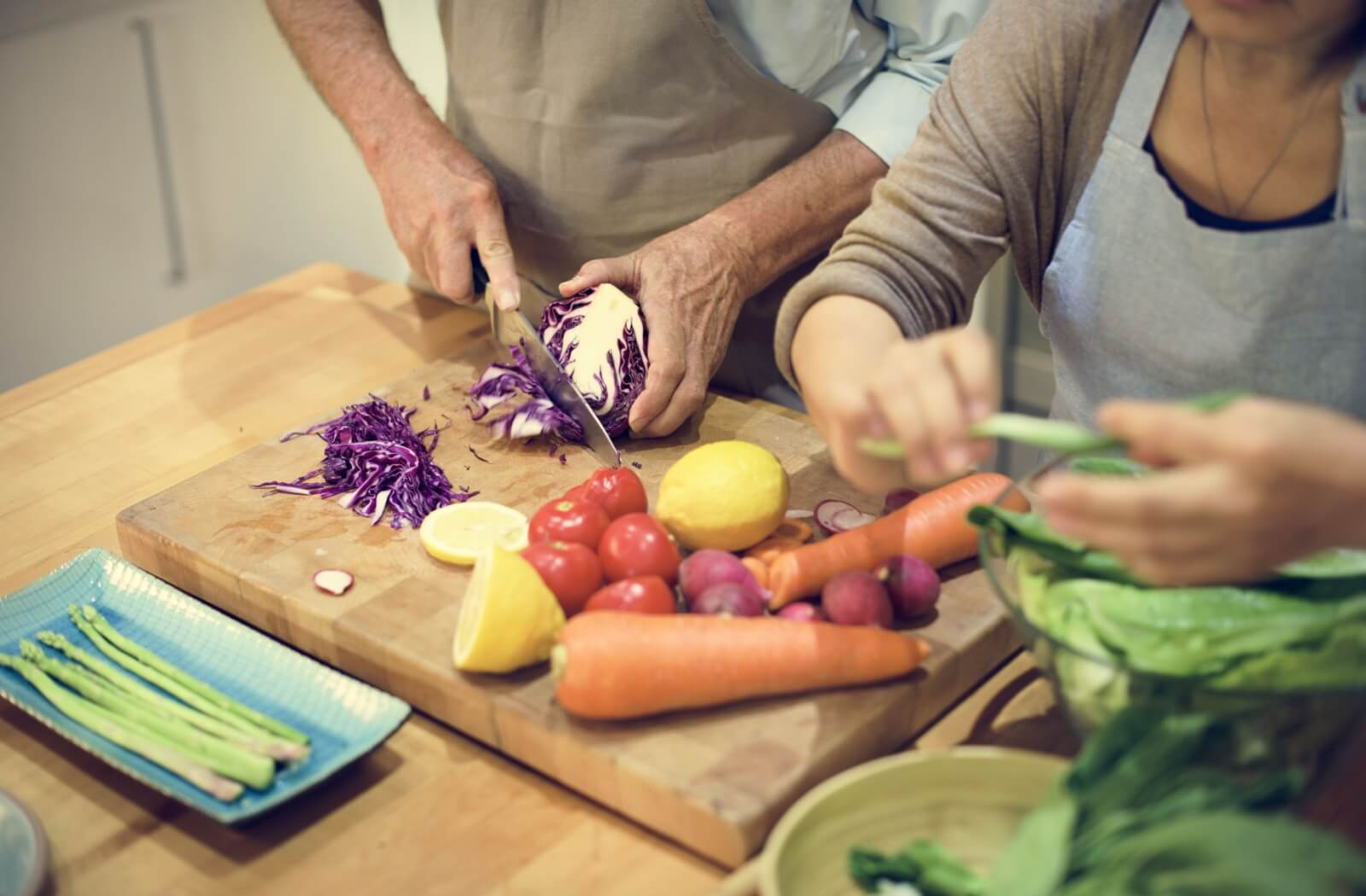 An older couple chops vegetables together for a nutritious salad