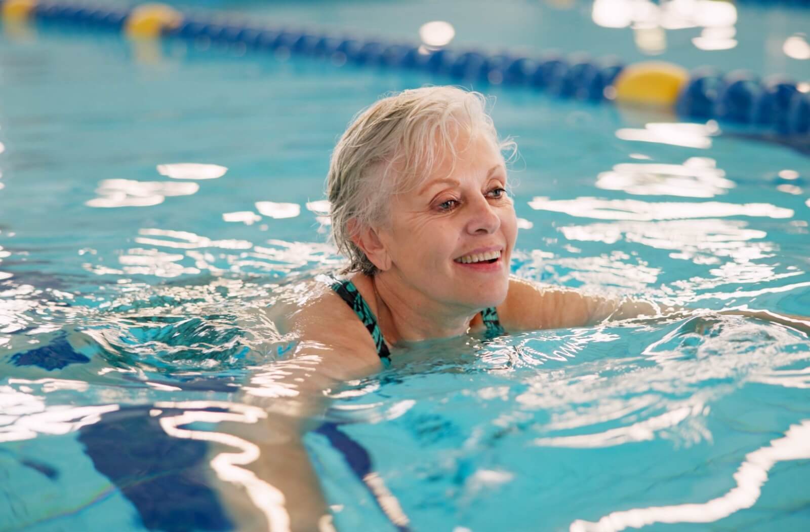 An older adult grins while swimming during aquatic therapy in their new senior living community