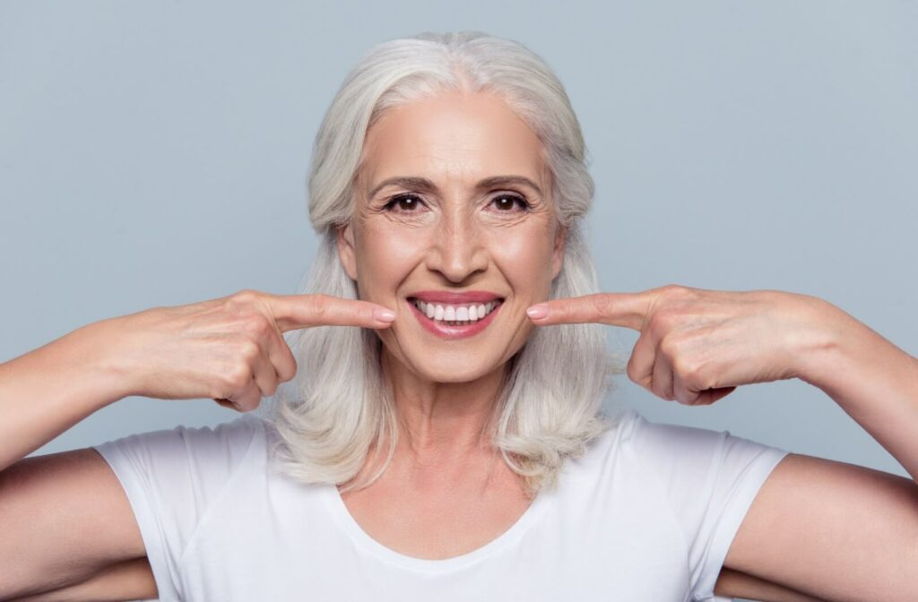 An older adult smiles and points to their bright white teeth after a dental exam