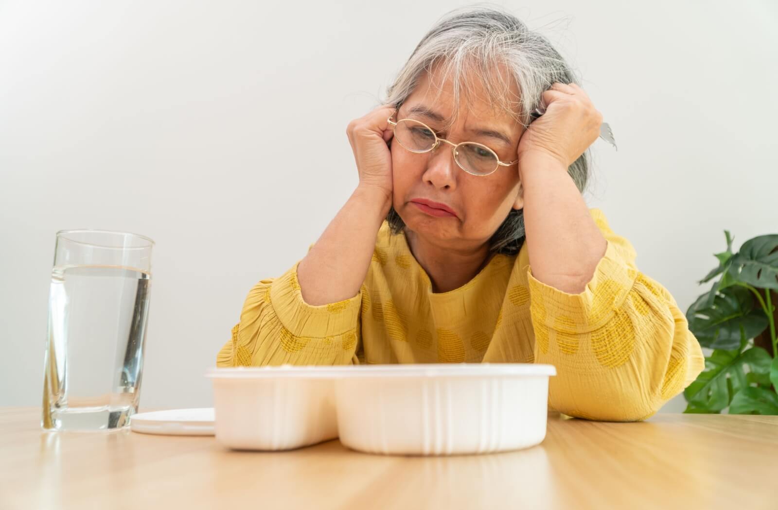 An older adult with dementia stares uninterested at a white bowl of food on their kitchen table