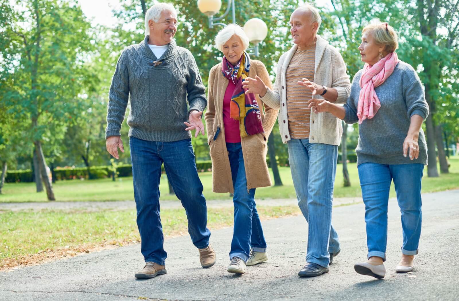 4 older adults walking together through a public park during a group outing, laughing and deep in conversation