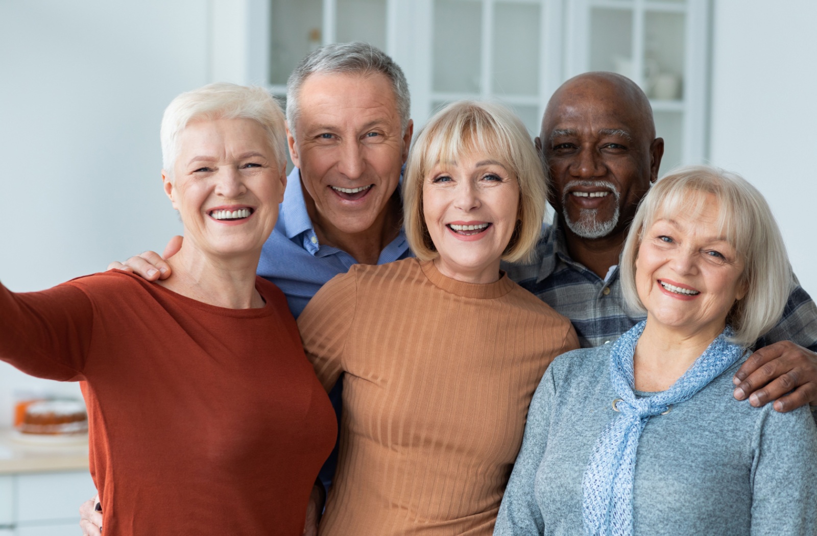A group of older adults in a senior living community holding each other and smiling.
