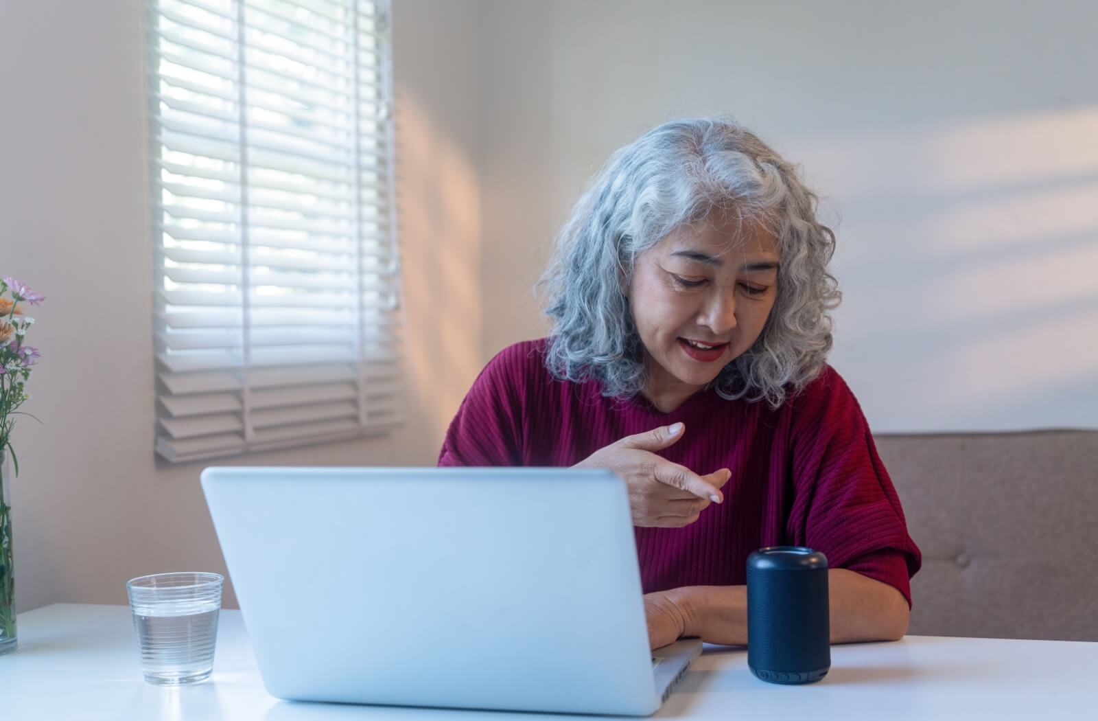 Older adult sitting at desk with laptop and using Alexa smart speaker in a bright room