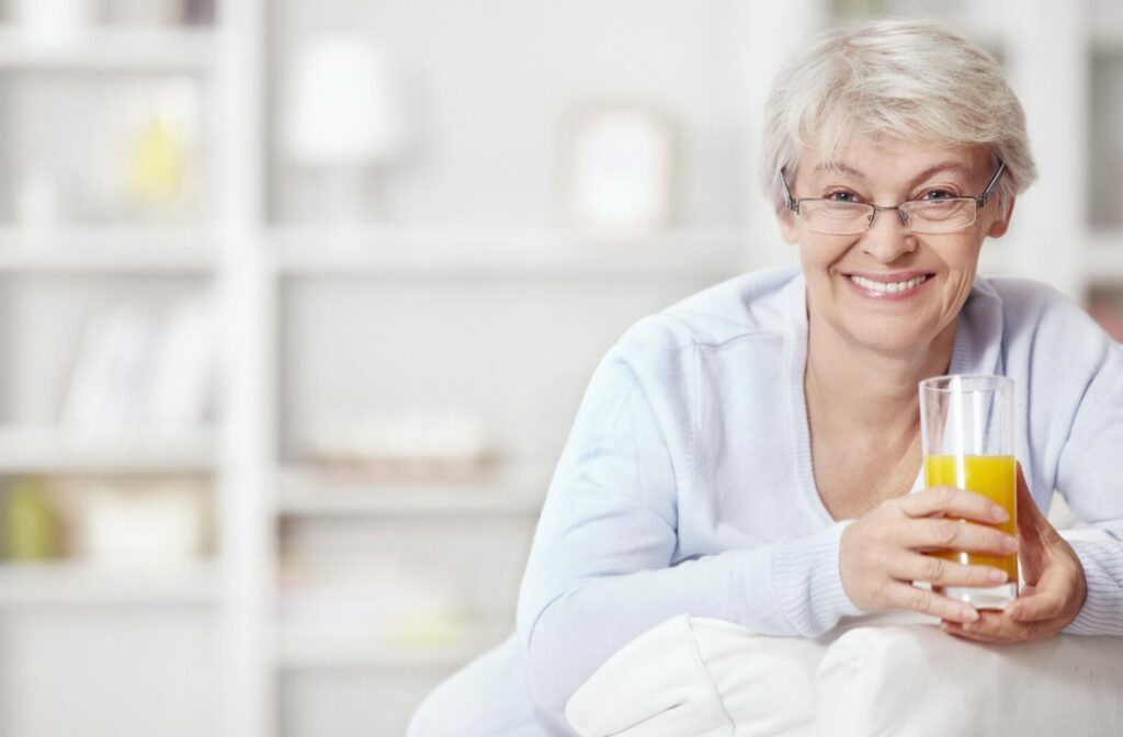 Smiling older adult holding a glass of orange juice at home enjoying healthy living and independence
