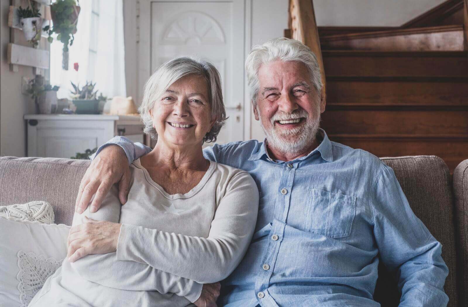 a senior couple sitting on the sofa smiling to camera