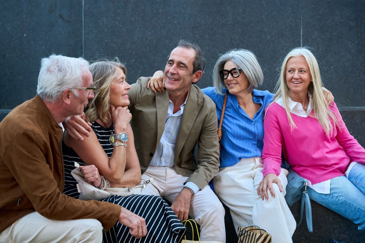 A group of seniors sitting beside each other wearing bright colours and laughing and smiling happily